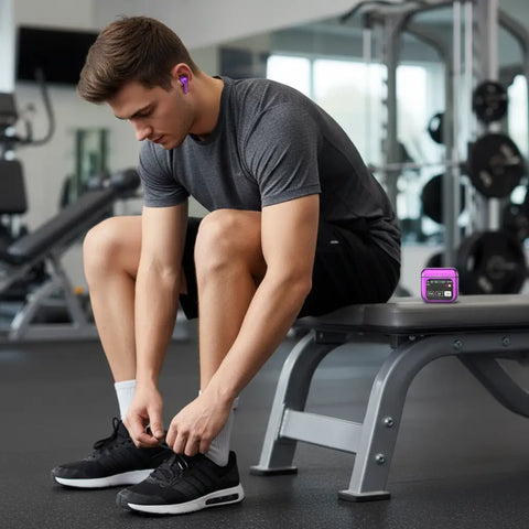 Hombre joven en gimnasio con auriculares inalámbricos Bluetooth negros puestos y estuche de carga con pantalla digital sobre un banco de entrenamiento