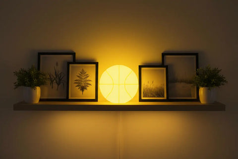 Lámpara circular amarilla de balón baloncesto que brilla en la oscuridad, en estantería con plantas y grabados