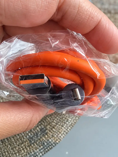 Cable de carga múltiple 4 en 1 naranja con conectores negros envuelto en plástico para uso en coche u oficina