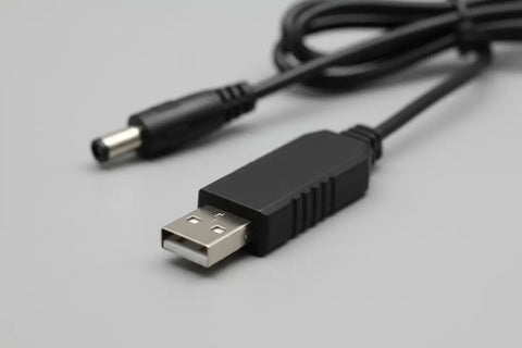 Cable USB a conector de corriente DC negro enrollado, visto en detalle sobre fondo blanco